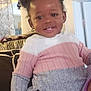 Maleah is registered to the contest to win money with this photo: toddler, child, smile, face, hair, pigtails, sweater, pink, gray, white, indoor, couch, happy, portrait, person, cute, young_child, hand, seated, cozy