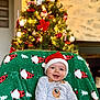 Lisandre a rejoint le concours — aidez-le/la à gagner de superbes lots ! baby, santa_hat, christmas_tree, holiday, festive, smiling, green_blanket, indoor, cozy, decorations, ornaments, lights, cute, infant, celebration, happy, christmas, seasonal, child, warm