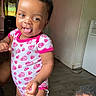 baby, child, indoor, onesie, heart_pattern, smiling, tongue_out, cute, person, portrait, happy, skin, hair, hand, floor, wall, doorway, light, furniture, head