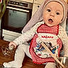 baby, child, apron, kitchen, whisk, wooden_spoon, bowl, cooking, cooking_utensils, face, expression, sitting, table, clothing, headwear, cute, indoors, person, light, gingham