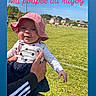 baby, child, pink_hat, polka_dot, outdoor, rugby_field, grass, blue_sky, clouds, hand, person_holding, sports, playing_field, daylight, people_in_background, casual_clothing, smiling, cute, hat, portrait