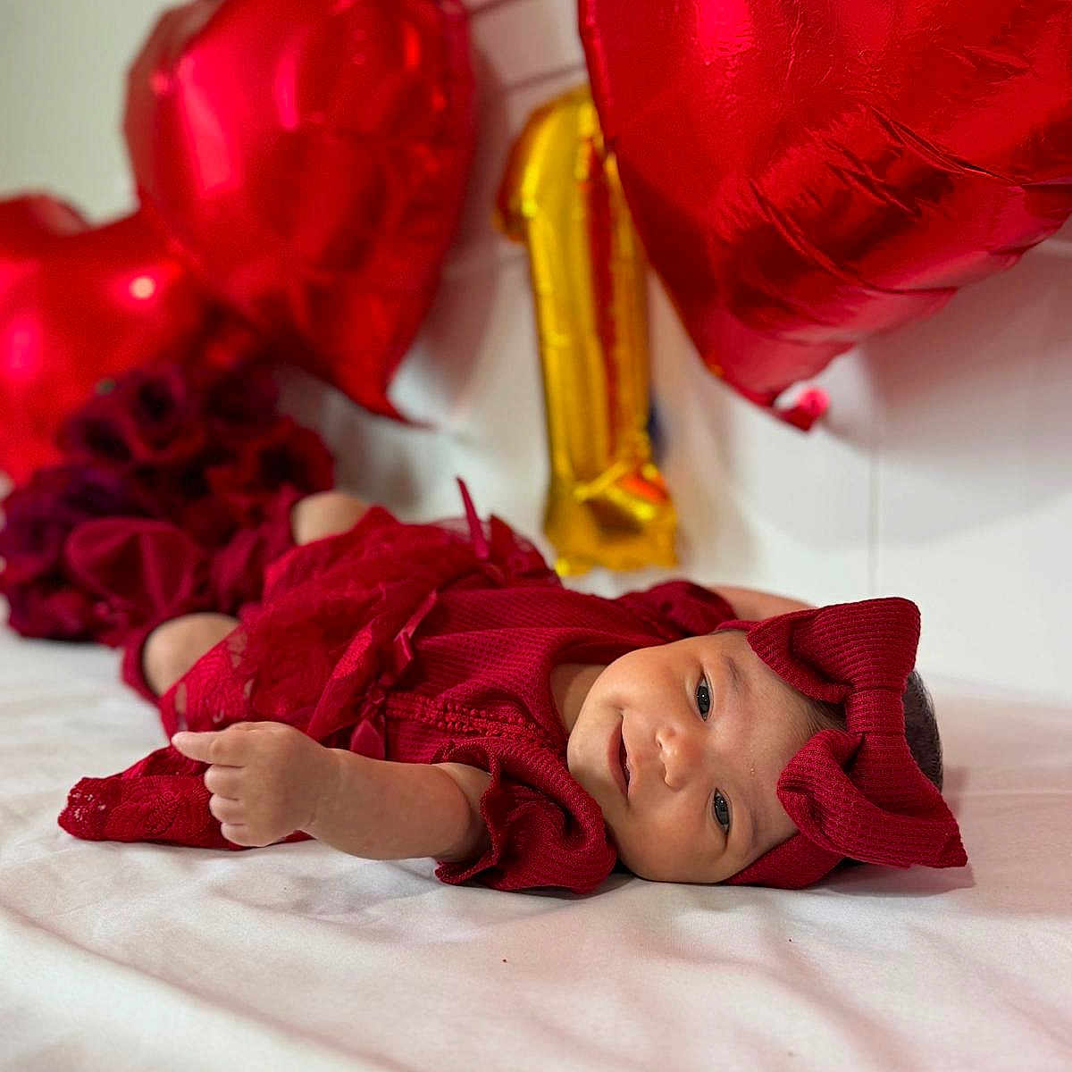 Allis is registered to the contest to win money with this photo: baby, infant, child, portrait, red_outfit, knitwear, bow, balloons, red_balloons, gold_balloon, bed, bedroom, lying_down, smiling, face, indoor, celebration, valentines_day, festive, photography