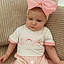 baby, child, pink_bow, headband, shirt, boss_text, couch, beige, clothing, infant, cute, portrait, sitting, indoors, soft_lighting, young_child, expression, person, fabric, comfortable