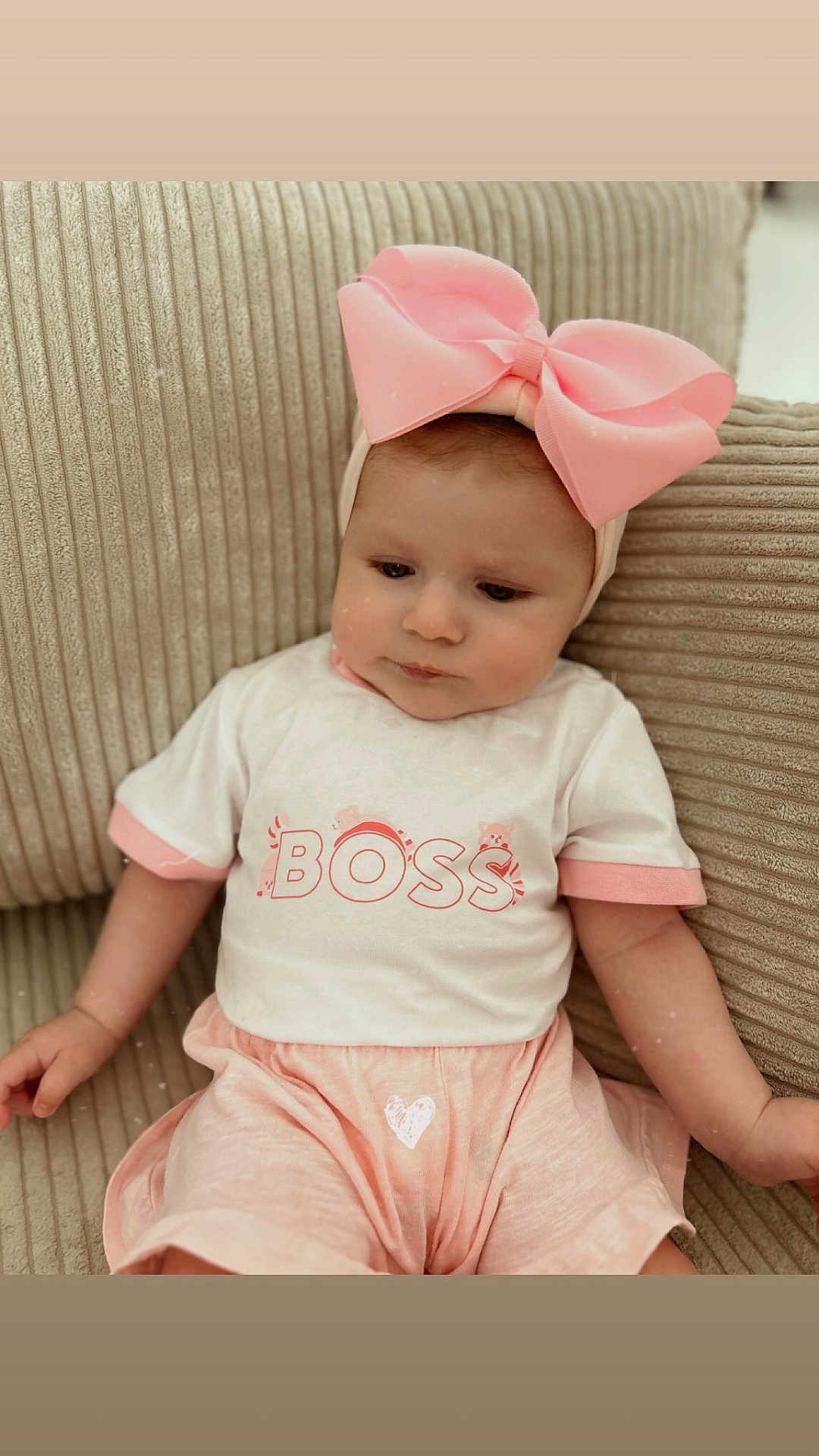 Carmen participe au concours pour gagner de l'argent avec cette photo : baby, child, pink_bow, headband, shirt, boss_text, couch, beige, clothing, infant, cute, portrait, sitting, indoors, soft_lighting, young_child, expression, person, fabric, comfortable