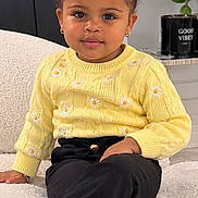 Maia is registered to the contest to win money with this photo: child, toddler, portrait, sitting, smiling, fashion, yellow_sweater, daisy, hair_bows, braided_hair, earrings, black_pants, couch, indoor, home, plant, decor, good_vibes, cozy, photography