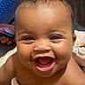 Maia is registered to the contest to win money with this photo: baby, child, infant, smiling, laughing, portrait, face, eyes, mouth, teeth, curly_hair, blanket, wrapped, sitting, indoor, home, close_up, happy, joyful, adorable