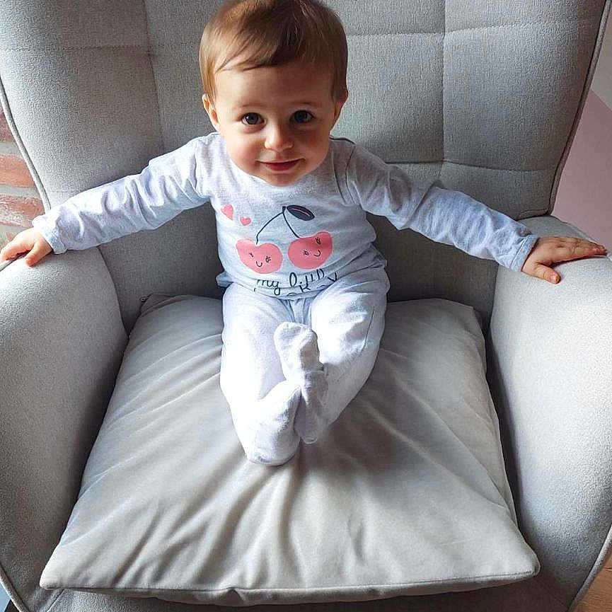 Lyson participe au concours pour gagner de l'argent avec cette photo : baby, child, clothing, cushion, cute, expression, eyes, furniture, gray, hair, indoor, long_sleeve, person, pillow, pink_rug, rocking_chair, sitting, smiling_face, toddler, wood_floor