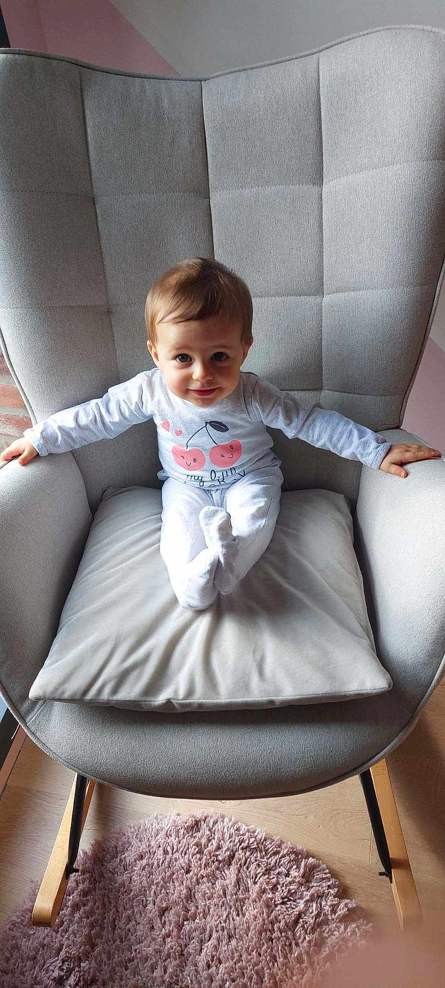 Lyson participe au concours pour gagner de l'argent avec cette photo : toddler, child, baby, rocking_chair, cushion, gray, pink_rug, wood_floor, clothing, long_sleeve, cute, smiling_face, indoor, furniture, pillow, person, hair, eyes, expression, sitting