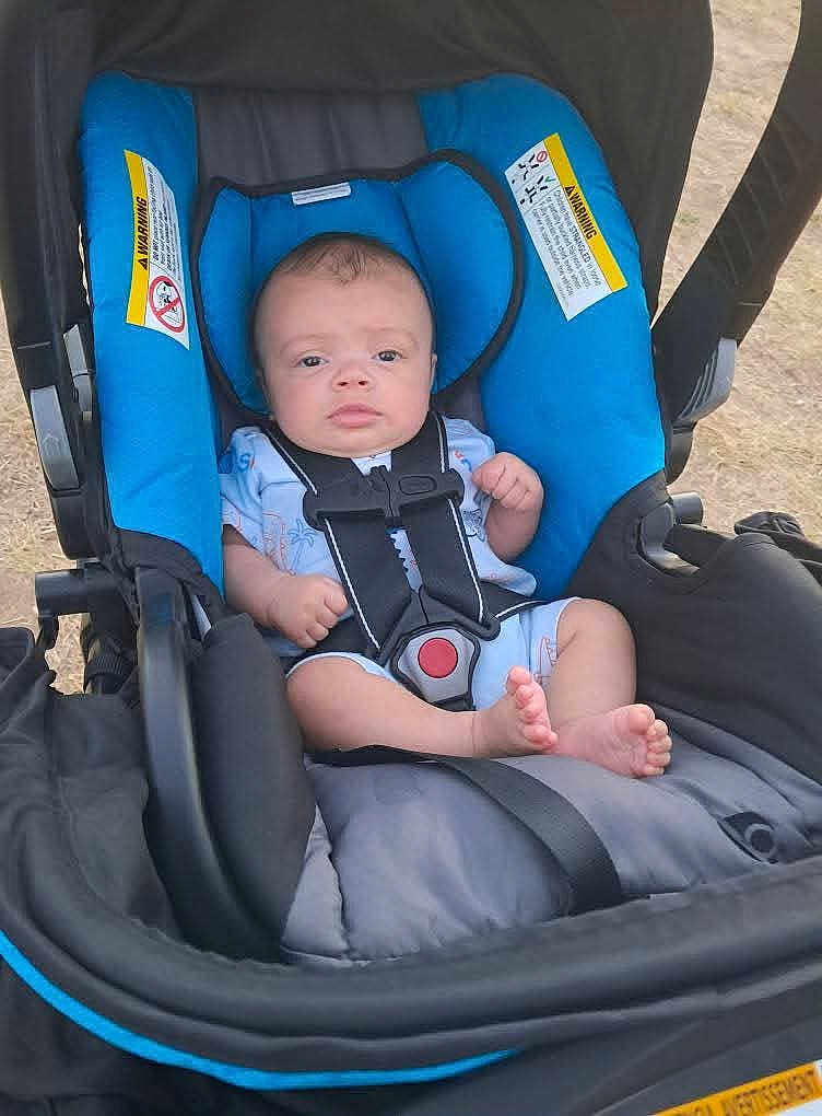William joined the competition — help win amazing prizes! baby, stroller, infant, child, blue, black, outdoor, seat, harness, foot, person, young_child, casual_clothing, head, expression, sitting, daylight, warning_label, fabric, comfort
