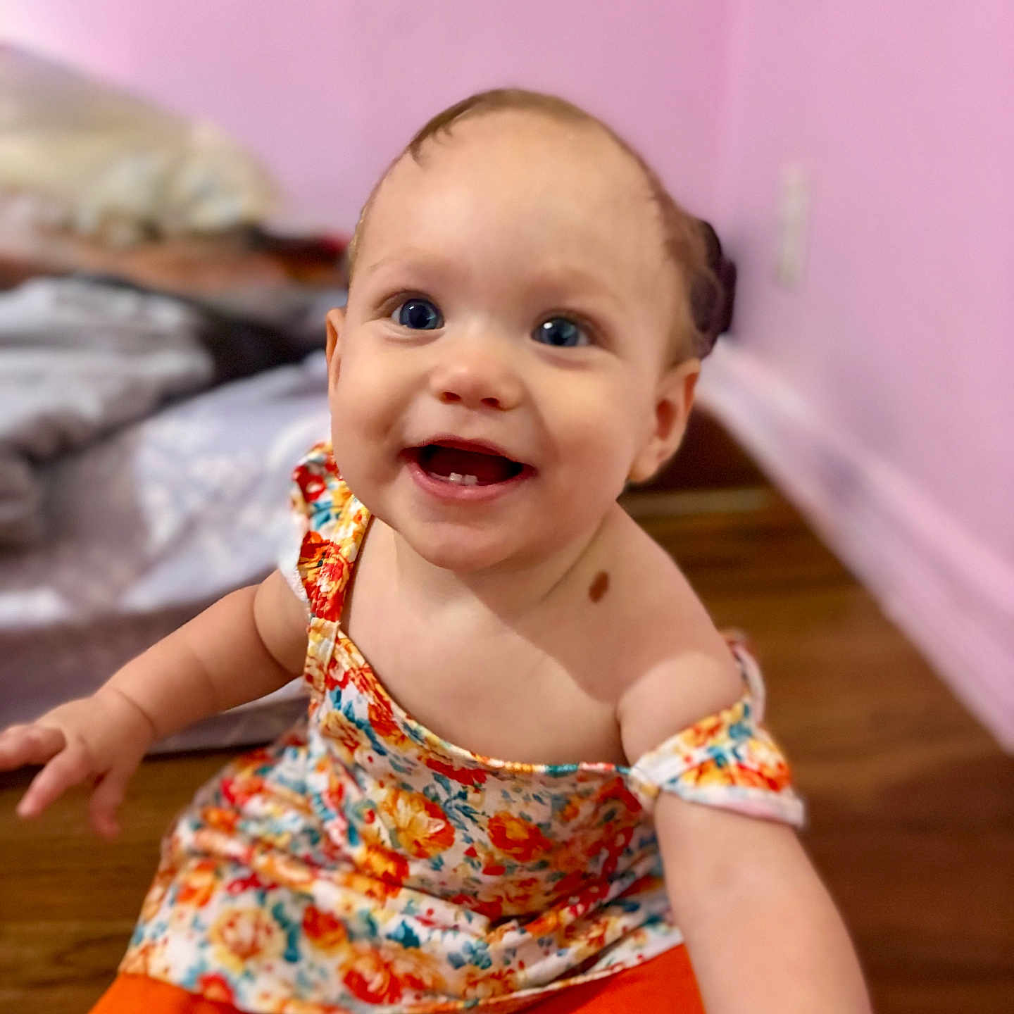 Omyra is registered to the contest to win money with this photo: arm, baby, blue_eyes, child, colorful_clothing, cute, floor, floral_pattern, happy, indoor, orange_shorts, person, pink_wall, portrait, sitting, skin, smiling, toddler, wall, wooden_floor