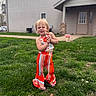 child, toddler, outdoor, grass, house, playful, smile, colorful_clothing, flower_pattern, striped_pants, greenery, young_child, happy, cute, person, daylight, casual, portrait, standing, fun
