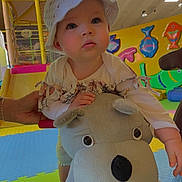 Giulia a rejoint le concours — aidez-le/la à gagner de superbes lots ! toddler, child, hat, plush_toy, indoor_play_area, colorful, play_mat, toy, hand, adult_hand, curious, face, expression, fish_wall_decoration, slide, crawling, floor, clothing, person, bright