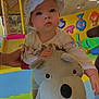 toddler, child, hat, plush_toy, indoor_play_area, colorful, play_mat, toy, hand, adult_hand, curious, face, expression, fish_wall_decoration, slide, crawling, floor, clothing, person, bright
