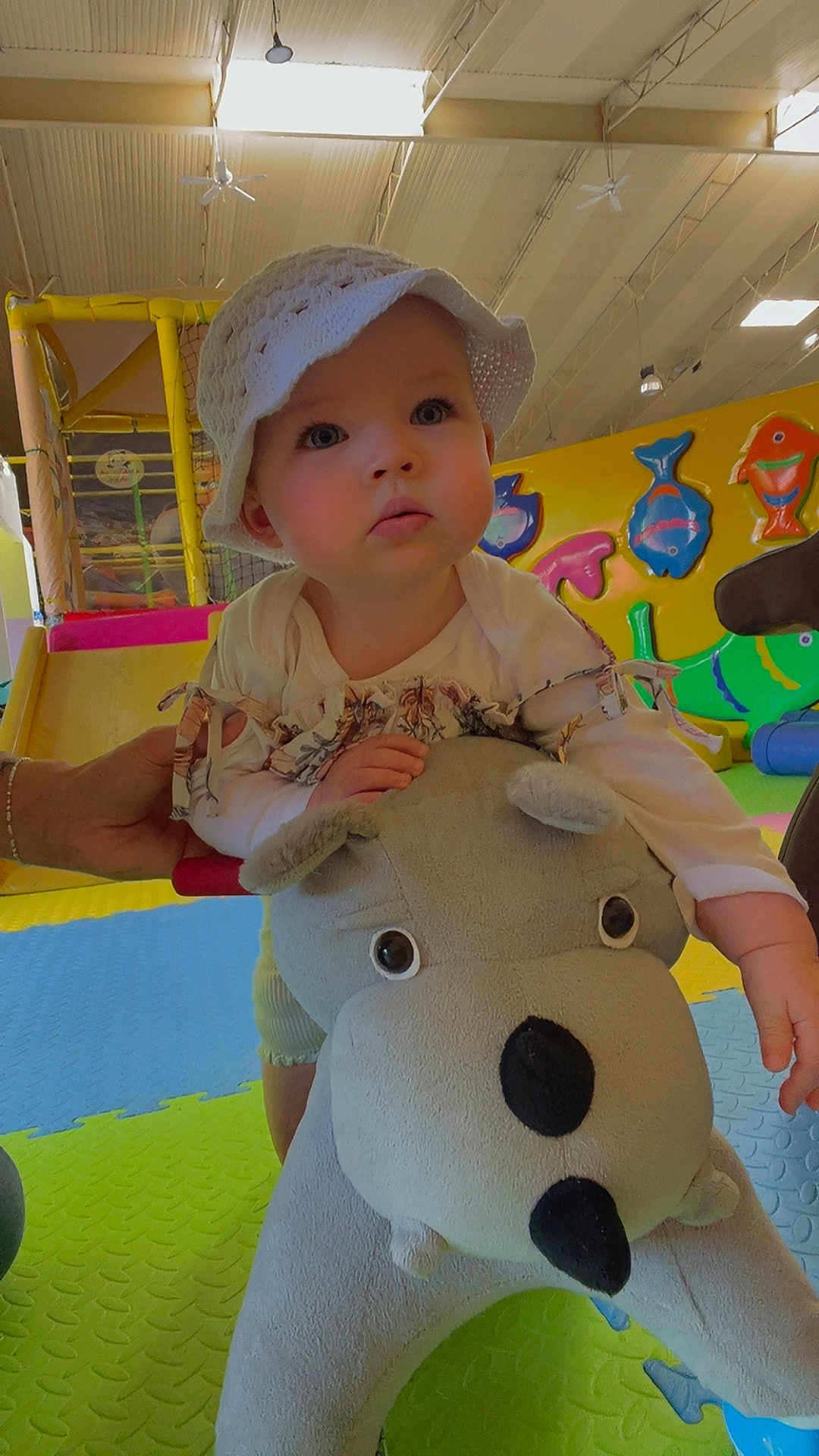 Giulia a rejoint le concours — aidez-le/la à gagner de superbes lots ! toddler, child, hat, plush_toy, indoor_play_area, colorful, play_mat, toy, hand, adult_hand, curious, face, expression, fish_wall_decoration, slide, crawling, floor, clothing, person, bright