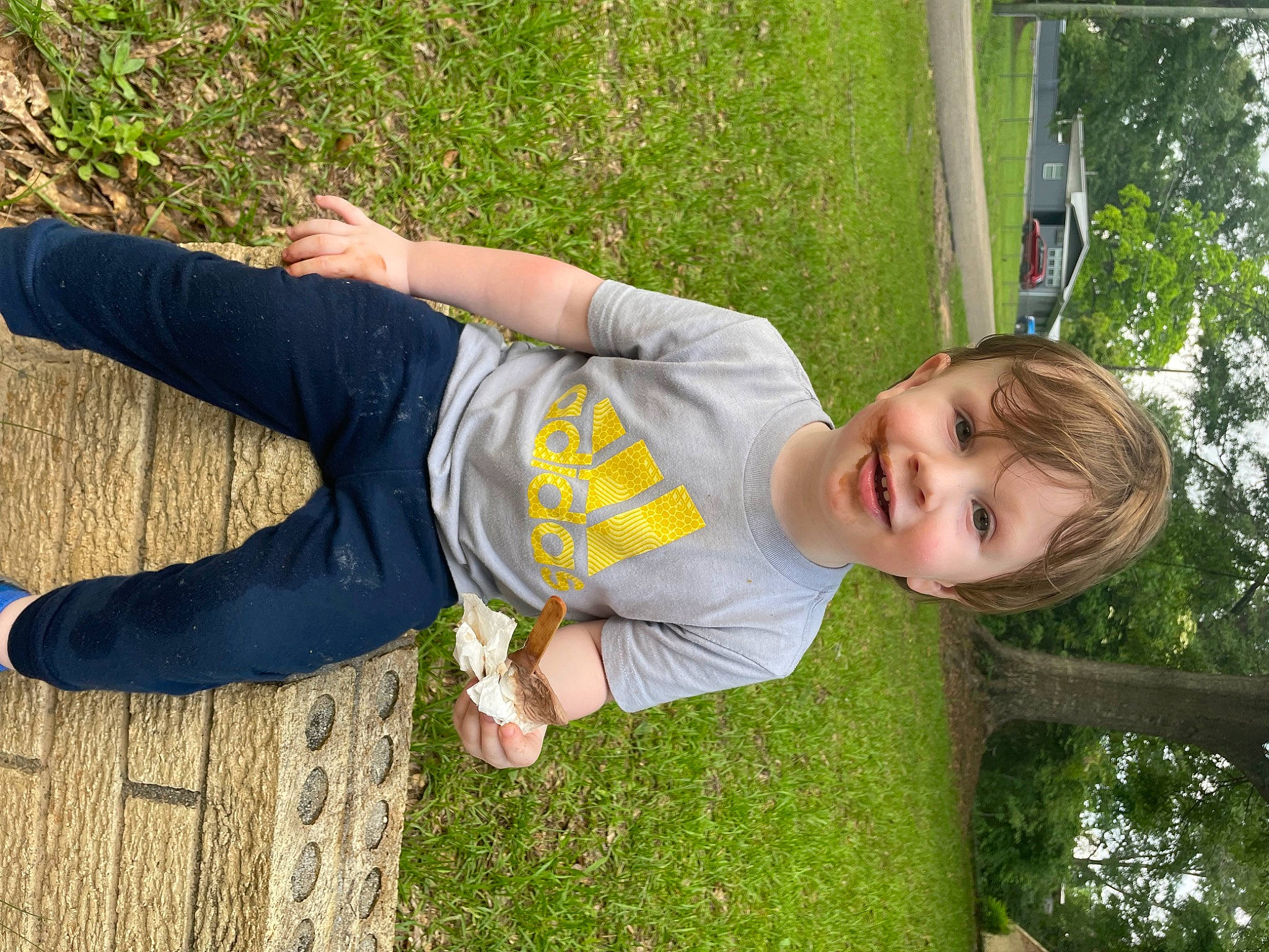 Austin is registered to the contest to win money with this photo: active_pants, child, elbow, fun, grass, happy, joy, knee, leisure, people_in_nature, person, plant, smile, sweatpant, t_shirt, thigh, toddler, tree, wood