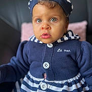 Isis participe au concours pour gagner de l'argent avec cette photo : baby, buttons, child, close_up, clothing, curly_hair, cute, eyes, face, gaze, hat, hooded_jacket, indoors, infant, navy_stripes, pillow, portrait, sitting, sofa, striped_dress