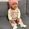 Isis a rejoint le concours — aidez-le/la à gagner de superbes lots ! baby, child, couch, cozy, cute, face, gray_couch, happy, indoor, patterned_clothing, person, pink_hat, pink_outfit, pom_pom, portrait, sitting, smiling, toddler, warm_clothing, white_socks
