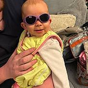 Lily participe au concours pour gagner de l'argent avec cette photo : baby, infant, child, sunglasses, smile, hand, adult_hand, bib, onesie, couch, pillow, blanket, living_room, portrait, person, accessory, bag, zipper, fabric, cozy