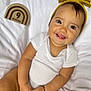 baby, infant, smiling, white_onesie, headband, yellow_bow, milestone_block, 9_months, wooden_block, blanket, soft_texture, happy, portrait, cute, child, sitting, hands, bracelet, indoors, closeup