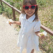 Inaya a rejoint le concours — aidez-le/la à gagner de superbes lots ! casual_wear, child, fence, flower, girl, greenery, hair, happy, nature, outdoor, person, playful, sandals, shadow, sidewalk, smile, summer, sunglasses, sunlight, white_dress