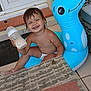 toddler, child, smiling, baby_bottle, inflatable, pool_float, outdoor, door, window, table, placemat, wicker, tile_floor, person_reflection, happy, bare_chest, diaper, footwear, toy, summer