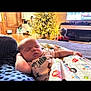 baby, sleeping, blanket, couch, living_room, christmas_tree, holiday, child, television, furniture, wood_floor, decorations, indoors, cozy, relaxing, person, patterned_clothing, home, resting, soft_lighting