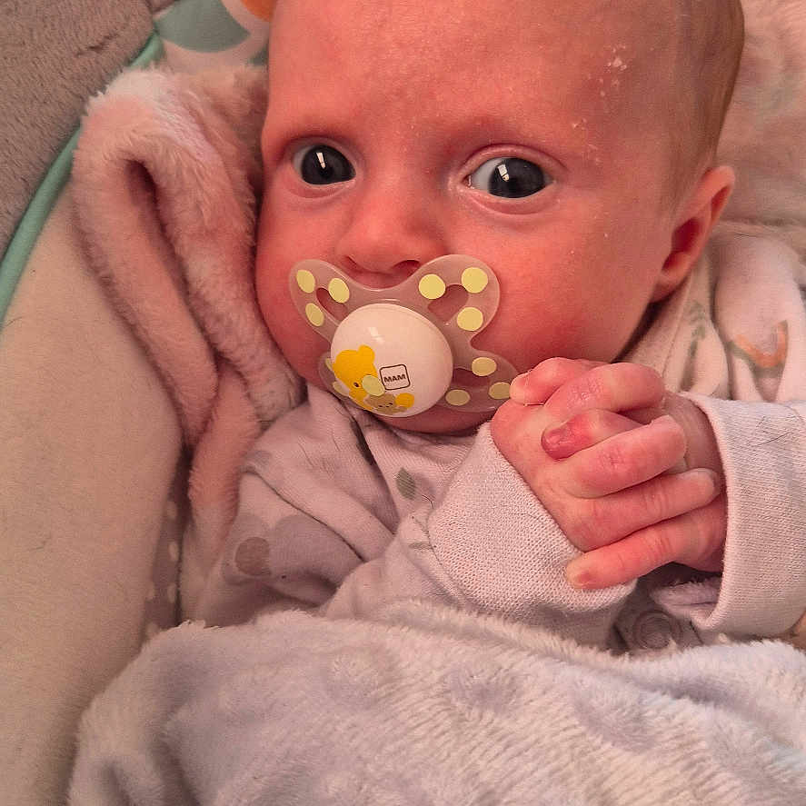 Raya-Louise is registered to the contest to win money with this photo: baby, blanket, child, closeup, clothing, comfort, cute, expression, face, hand, indoor, infant, newborn, pacifier, peaceful, portrait, rest, skin, sleeping_bag, soft_texture