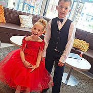Britney participe au concours pour gagner de l'argent avec cette photo : child, boy, girl, red_dress, black_vest, bow_tie, smile, indoor, carpet, table, chair, cushion, window, glass, shoe, floor, person, portrait, happy, formal_wear