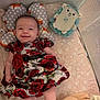 baby, infant, smiling, dress, red_roses, pillow, fox_pattern, plush_toy, blue_plush, blanket, floral_pattern, playpen, mesh_sides, soft_bedding, indoor, cute, happy, child, laying_down, cozy