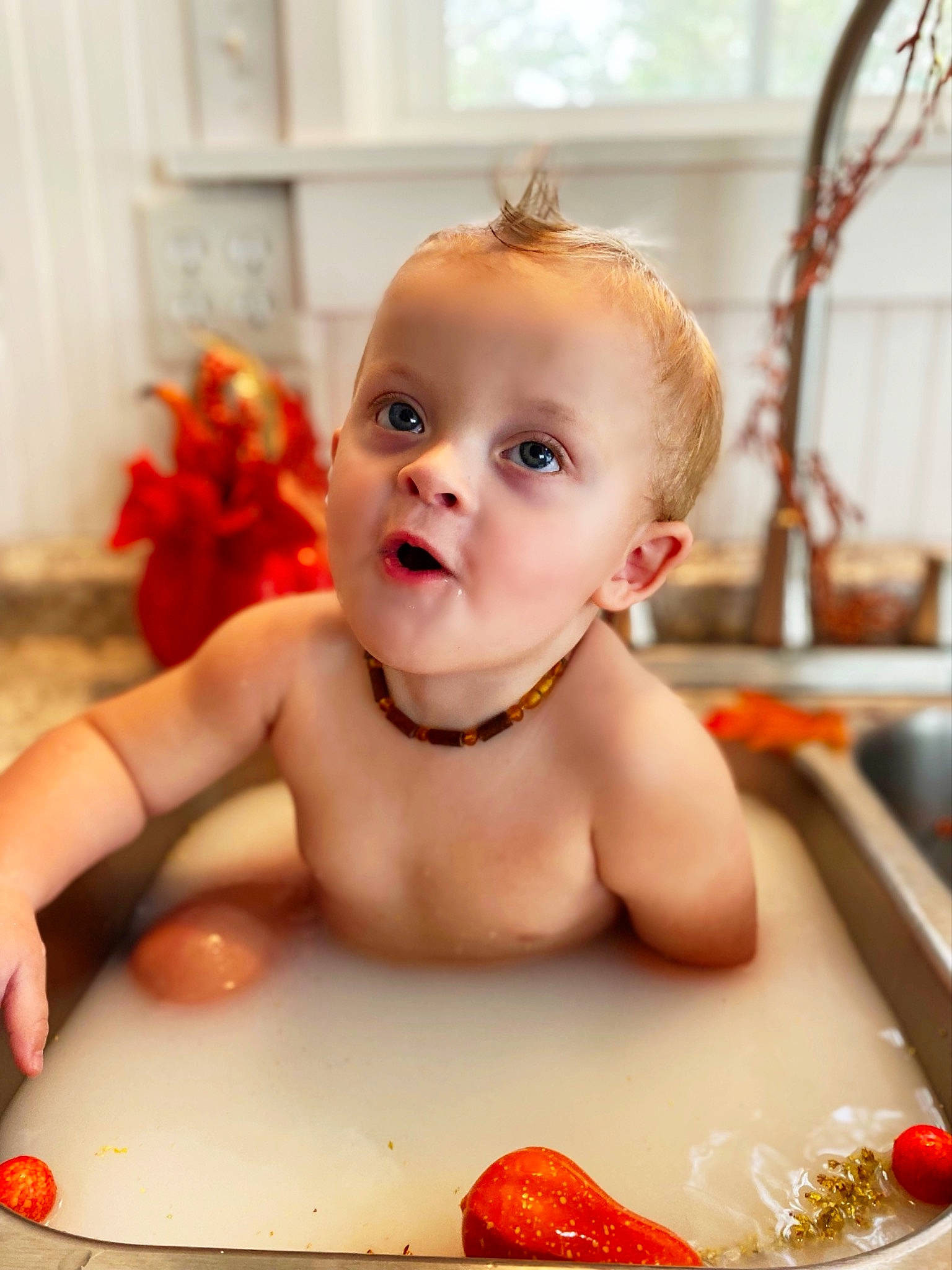 Kolten is registered to the contest to win money with this photo: arm, baby, bathing, cheek, chest, eye, eyelash, face, finger, human_body, lip, mouth, nose, orange, person, plumbing_fixture, red, skin, smile, toddler