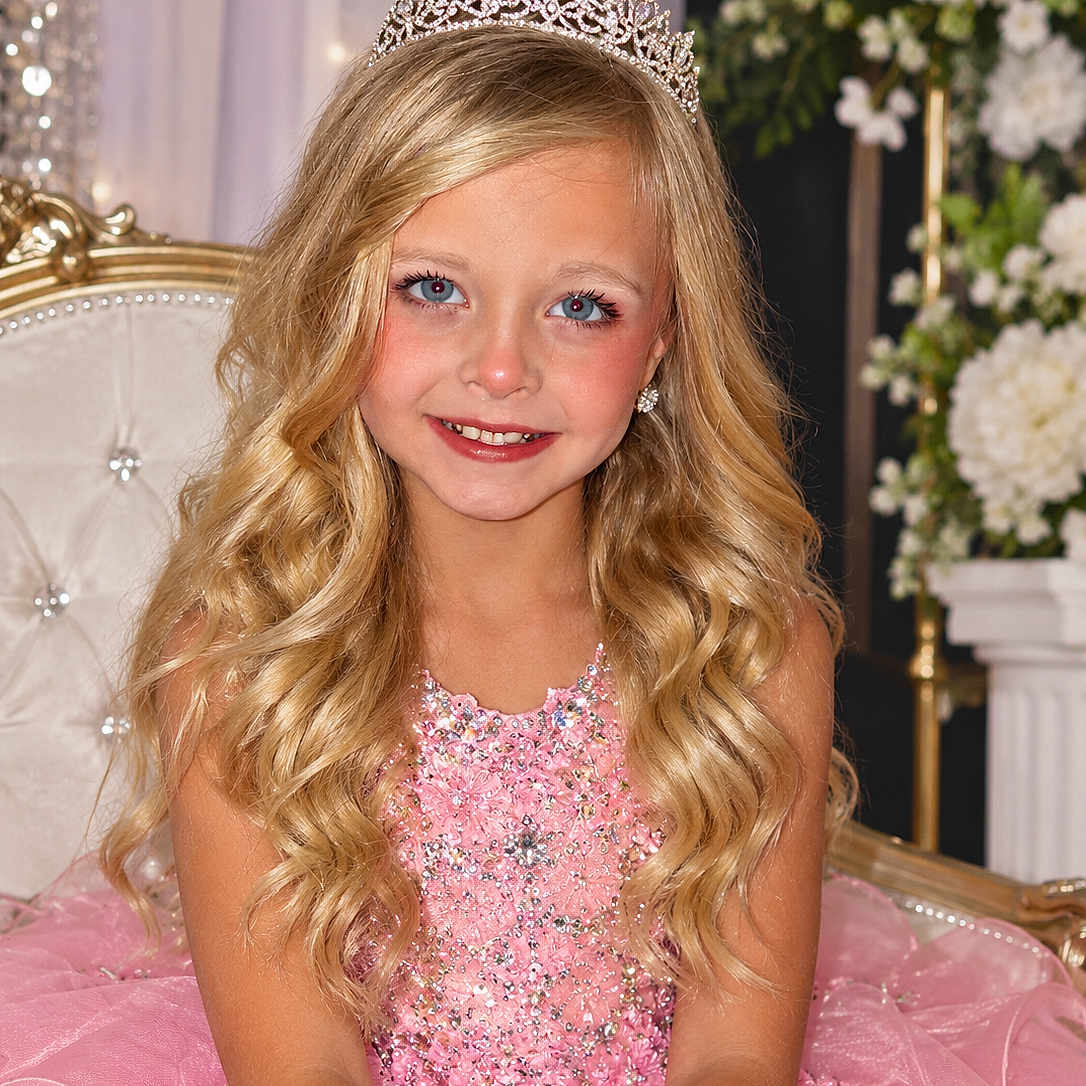 Presley is registered to the contest to win money with this photo: child, girl, smiling, portrait, tiara, princess, pink_dress, sparkly, formalwear, blonde_hair, curly_hair, blue_eyes, earrings, seated, chair, floral_background, flowers, indoor, celebration, close_up