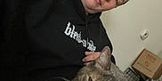 Princess is registered to the contest to win money with this photo: person, cat, indoor, hoodie, gray_cat, relaxed, seated, feline, pet, casual, home, whiskers, face, animal, comfort, box, cage, thermostat, black_clothing, resting