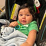 Abel is registered to the contest to win money with this photo: baby, child, infant, car_seat, blanket, toy, keys, green_shirt, face, hand, curly_hair, indoor, warning_label, cute, smiling, person, portrait, closeup, comfort, seat