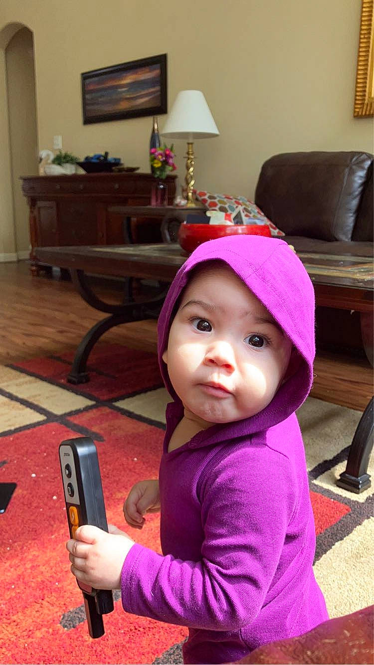 Athena is registered to the contest to win money with this photo: baby_toddler_clothing, cap, child, communication_device, gadget, headwear, lamp, living_room, magenta, mobile_phone, person, picture_frame, pink, portable_communications_device, room, skin, standing, table, telephone, telephony