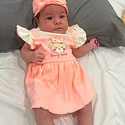 Rebecca joined the competition — help win amazing prizes! baby, infant, child, dress, headband, bow, pink, peach, cute, lying_down, pillow, white_sheet, clothing, portrait, young_child, indoors, skin, face, arms, legs