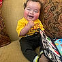 toddler, child, smiling, curly_hair, yellow_shirt, mickey_mouse, black_pants, sitting, couch, patterned_cushion, book, colorful, happy, indoors, feet, hand, toy, playful, cozy, portrait