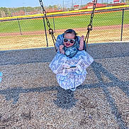 Dallas joined the competition — help win amazing prizes! baby, swing, playground, sunglasses, child, smiling, outdoor, woodchips, fence, sport_field, daylight, happy, casual_clothing, seat, metal_chains, green_grass, blue_sky, recreation, fun, park
