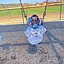 baby, swing, playground, sunglasses, child, smiling, outdoor, woodchips, fence, sport_field, daylight, happy, casual_clothing, seat, metal_chains, green_grass, blue_sky, recreation, fun, park