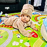 animal_illustrations, baby, carpet, child, colorful, couch, cozy_clothing, curious, cute, face, floor, hat, indoor, infant, person, play_mat, soft_toys, teddy_bear_patch, toddler, toy