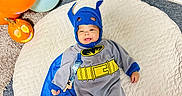 Noyer is registered to the contest to win money with this photo: baby, balloons, batman, blue, cape, carpet, carved, child, costume, cute, face, floor, gray, happy, indoors, infant, mat, pumpkin, smile, toy