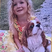 Vanina participe au concours pour gagner de l'argent avec cette photo : child, girl, dog, cavalier_king_charles_spaniel, pet, portrait, outdoor, garden, grass, path, floral_dress, blonde_hair, curly_hair, smiling, sitting, companion, long_ears, brown_and_white, daylight, family