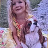 child, girl, dog, cavalier_king_charles_spaniel, pet, portrait, outdoor, garden, grass, path, floral_dress, blonde_hair, curly_hair, smiling, sitting, companion, long_ears, brown_and_white, daylight, family