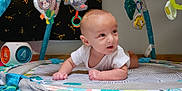 Chester is registered to the contest to win money with this photo: baby, infant, play_mat, activity_gym, toys, plush_toys, indoor, floor, curious, child, white_clothing, colorful, soft_lighting, head, hands, wooden_floor, baby_play, baby_toys, baby_gym, crawling