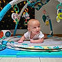 baby, infant, play_mat, activity_gym, toys, plush_toys, indoor, floor, curious, child, white_clothing, colorful, soft_lighting, head, hands, wooden_floor, baby_play, baby_toys, baby_gym, crawling