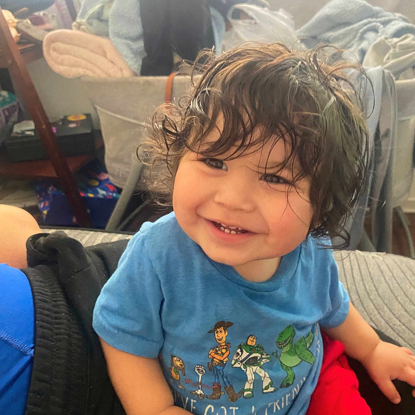 Isaiah is registered to the contest to win money with this photo: toddler, child, smiling, curly_hair, blue_shirt, red_shorts, indoor, blankets, furniture, happy, person, cute, casual_clothing, portrait, seated, home, toy_story, short_sleeves, young_child, playful