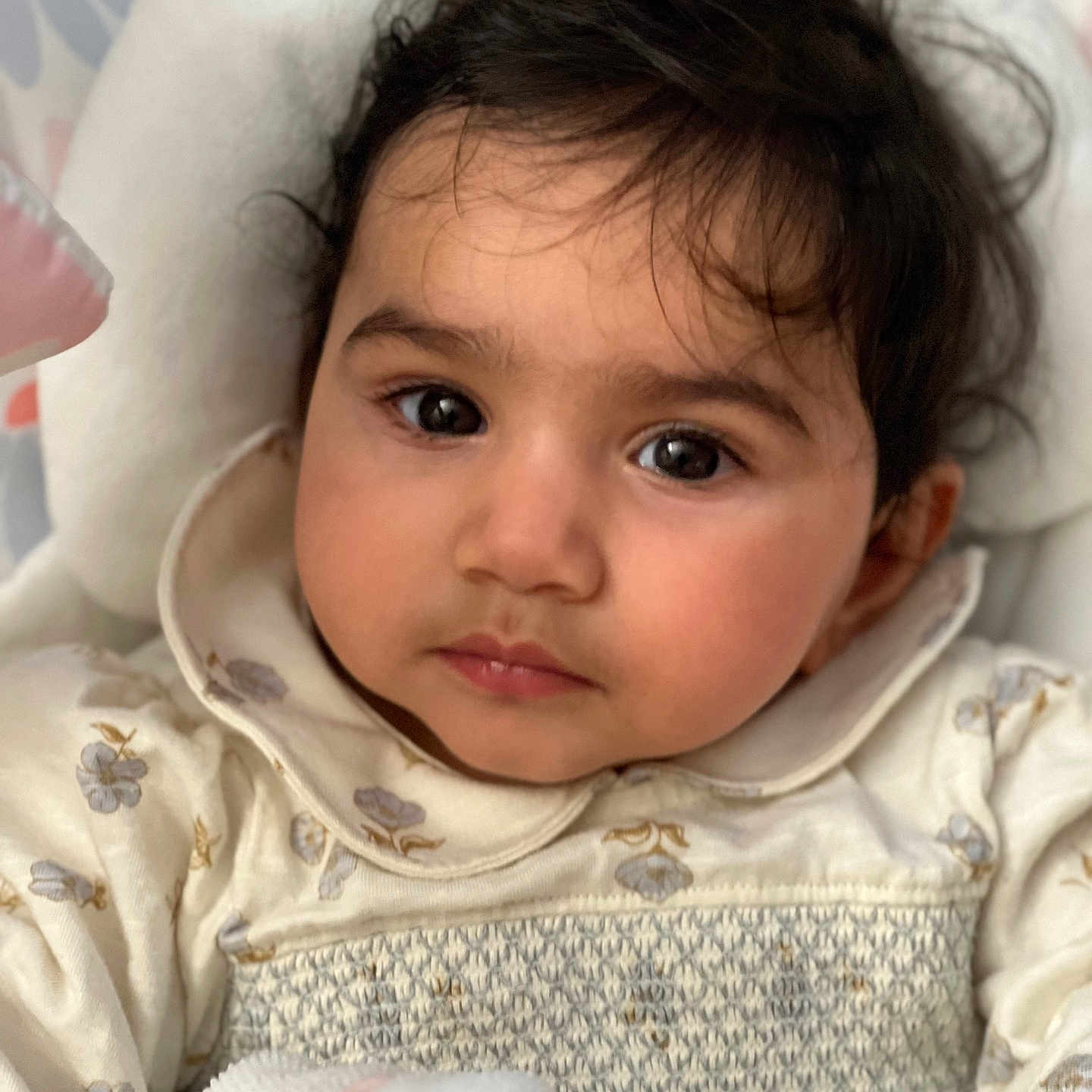 Ira is registered to the contest to win money with this photo: baby, child, portrait, face, eyes, hair, clothing, floral_pattern, blanket, cushion, soft_texture, indoor, cute, infant, closeup, skin, expression, resting, young, person