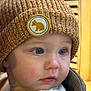 baby, child, face, blue_eyes, knit_hat, brown_hat, bear_patch, closeup, rosy_cheeks, soft_clothing, portrait, cute, indoors, warm_lighting, headwear, infant, looking_away, expression, person, young_child