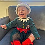 baby, child, smiling, holiday_outfit, santa_hat, candy_cane, red_socks, green_dress, bow, couch, indoor, window, plants, happy, cute, portrait, toddler, festive, cozy, celebration