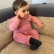 Zeyneb a rejoint le concours — aidez-le/la à gagner de superbes lots ! baby, child, pink_clothing, knitwear, socks, sofa, couch, indoor, curly_hair, cute, seated, portrait, cozy, textured_fabric, looking_sideways, hand_near_face, young_child, comfortable, soft_lighting, casual