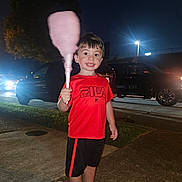 Greyson is registered to the contest to win money with this photo: child, boy, cotton_candy, red_shirt, black_shorts, sidewalk, night, streetlights, cars, grass, smile, short_hair, outdoor, holding, food, happy, casual_clothing, person, recreation, evening